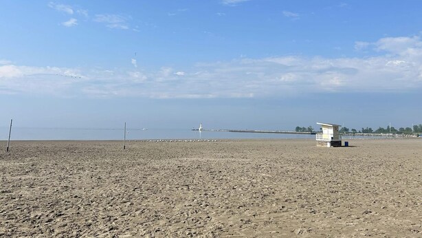 A beach with a lifeguard tower, a pier in the distance, and a clear sky. - The Poplars Suite 1827: A Historic Stay (Cobourg)