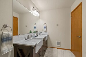 A bathroom with a double sink, a large mirror, and a wooden door. - Mountain Home in Coeur d’ Alene (Coeur d'Alene)