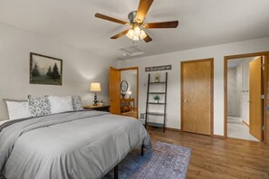 A bedroom with a bed, a ceiling fan, a nightstand, a lamp, a ladder, a door, and a shower area. - Mountain Home in Coeur d’ Alene (Coeur d'Alene)