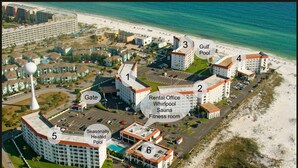 An aerial view of a hotel with amenities including a beach, tennis and pickle ball courts, a seasonal heated pool, and a rental office with a whirlpool, sauna, and fitness room.