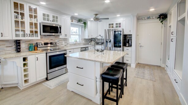 A modern kitchen with white cabinetry, a central island, stainless steel appliances, and a ceiling fan.