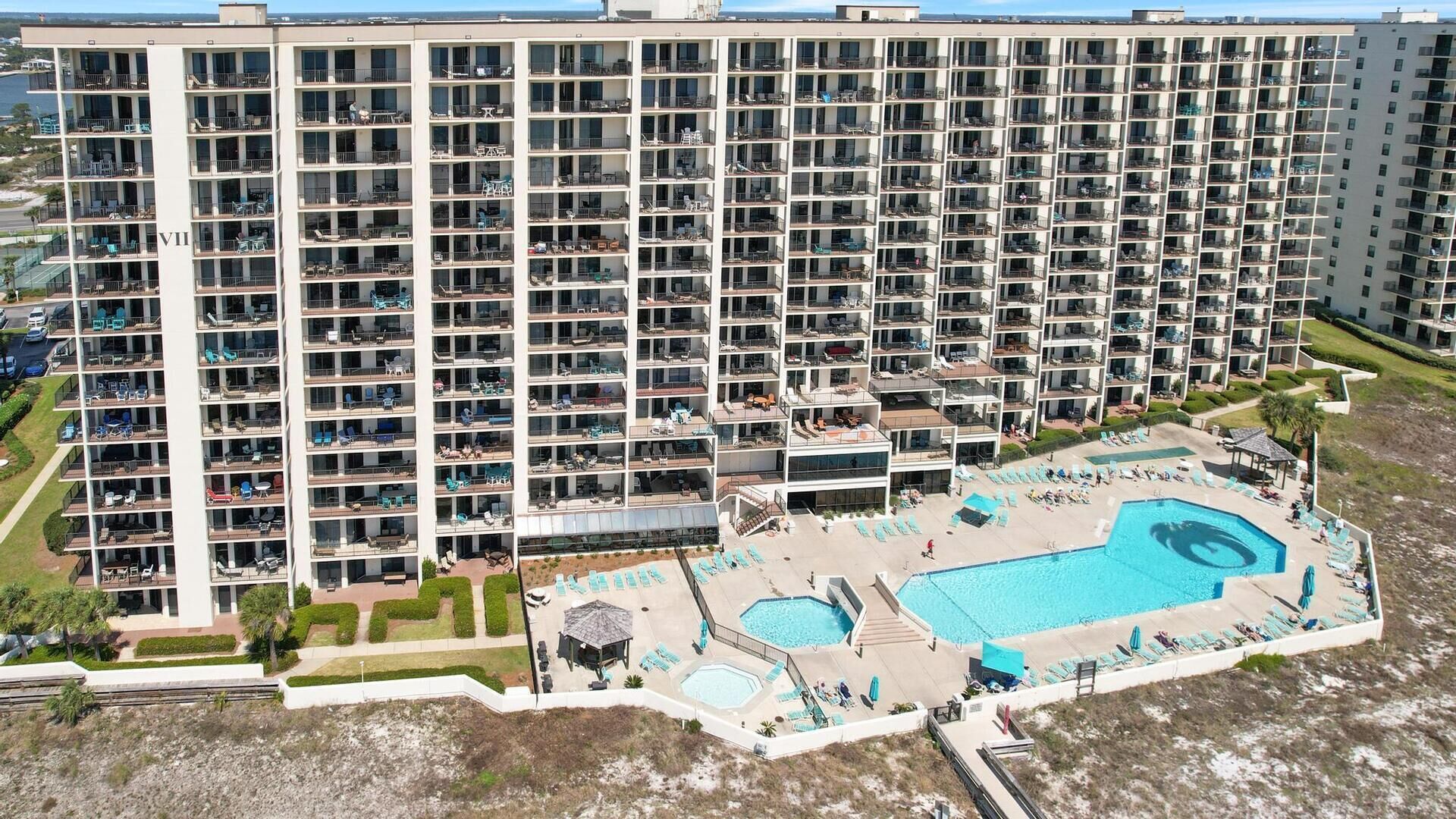 A high-rise hotel with multiple balconies, a swimming pool, and a landscaped area.