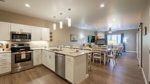 A modern kitchen with stainless steel appliances, a dishwasher, and a dining area with white chairs and a table.