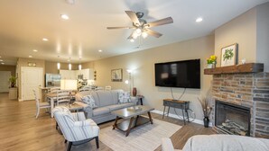 A spacious living room with a fireplace, a flat-screen TV, and a ceiling fan.