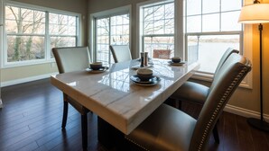 A dining area with a marble table, leather chairs, and a view of a lake through large windows.