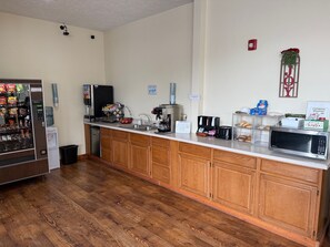 Een kitchenette met een koffieapparaat, magnetron en automaat.