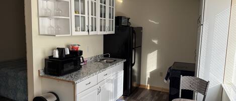 A compact kitchen with white cabinets, a black refrigerator, and a microwave.