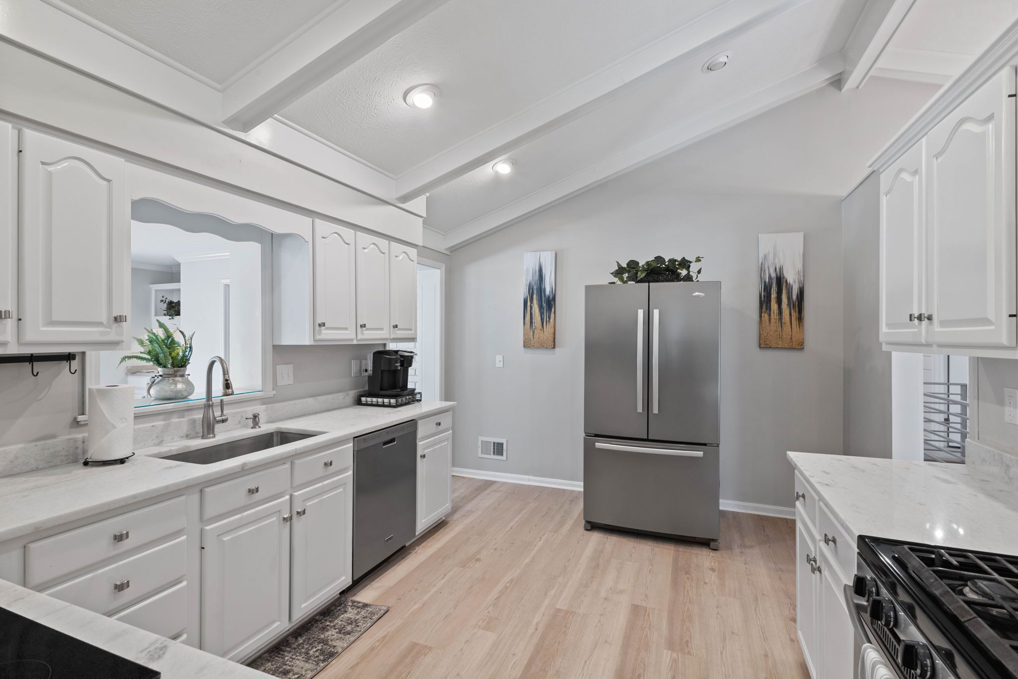 A modern kitchen with white cabinetry, stainless steel appliances, and a marble countertop.