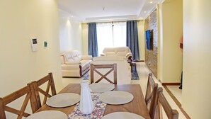 A dining area with a wooden table, chairs, and a vase. There is a sofa and a chair in the background. - Luxurious 2BR Retreat with Upscale Touches and 24/7 Security (Nairobi)