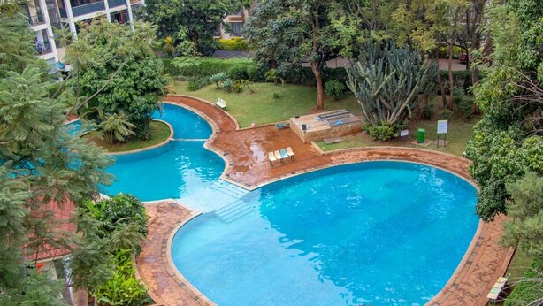 A large, curved swimming pool surrounded by lush greenery and a small deck area with lounge chairs. - Luxurious 2BR Retreat with Upscale Touches and 24/7 Security (Nairobi)