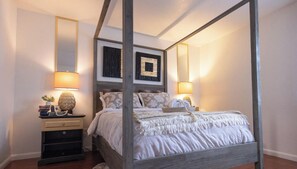 A four-poster bed with a wooden frame, a bedside table with a lamp, and a wall-mounted mirror. - Diamond In The Rough (Oakland)