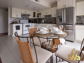 A modern kitchen with white cabinetry, a stainless steel refrigerator, and a round glass table set for dining.