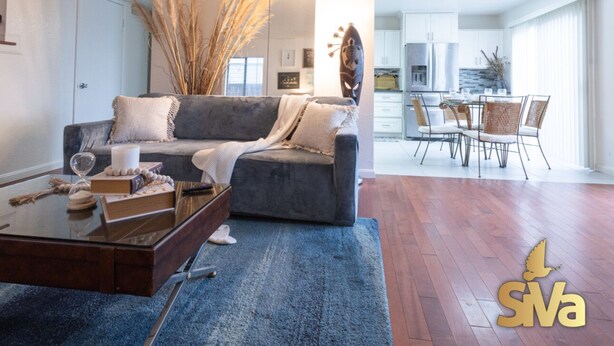 A modern living room with a grey sofa, a coffee table with books and a glass, and a dining area with a table and chairs. - Diamond In The Rough (Oakland)