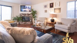 A living room with a fireplace, a television, and a comfortable seating area. - Diamond In The Rough (Oakland)