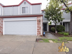 A residential house with a garage, a brick facade, and a tree in the front yard.