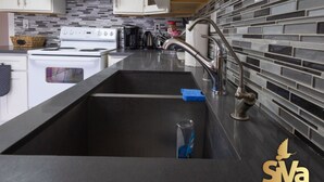 A modern kitchen with a stainless steel sink, white cabinets, and a tiled backsplash. - Diamond In The Rough (Oakland)