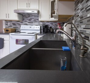 A modern kitchen with a stainless steel sink, white cabinets, and a tiled backsplash. - Diamond In The Rough (Oakland)