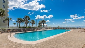 A rectangular swimming pool with a tiled deck, surrounded by palm trees and a white fence. - Beach View 3br/2ba W/pools Sleeps 8 (Orange Beach)