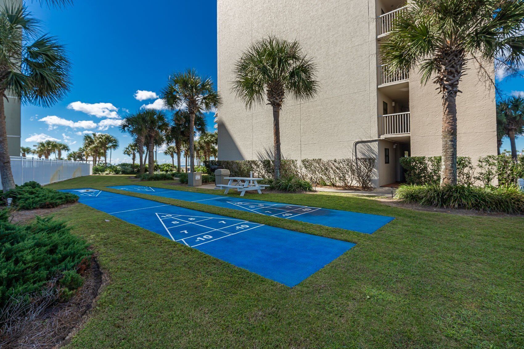 A courtyard with a shuffleboard court, palm trees, and a building with balconies.