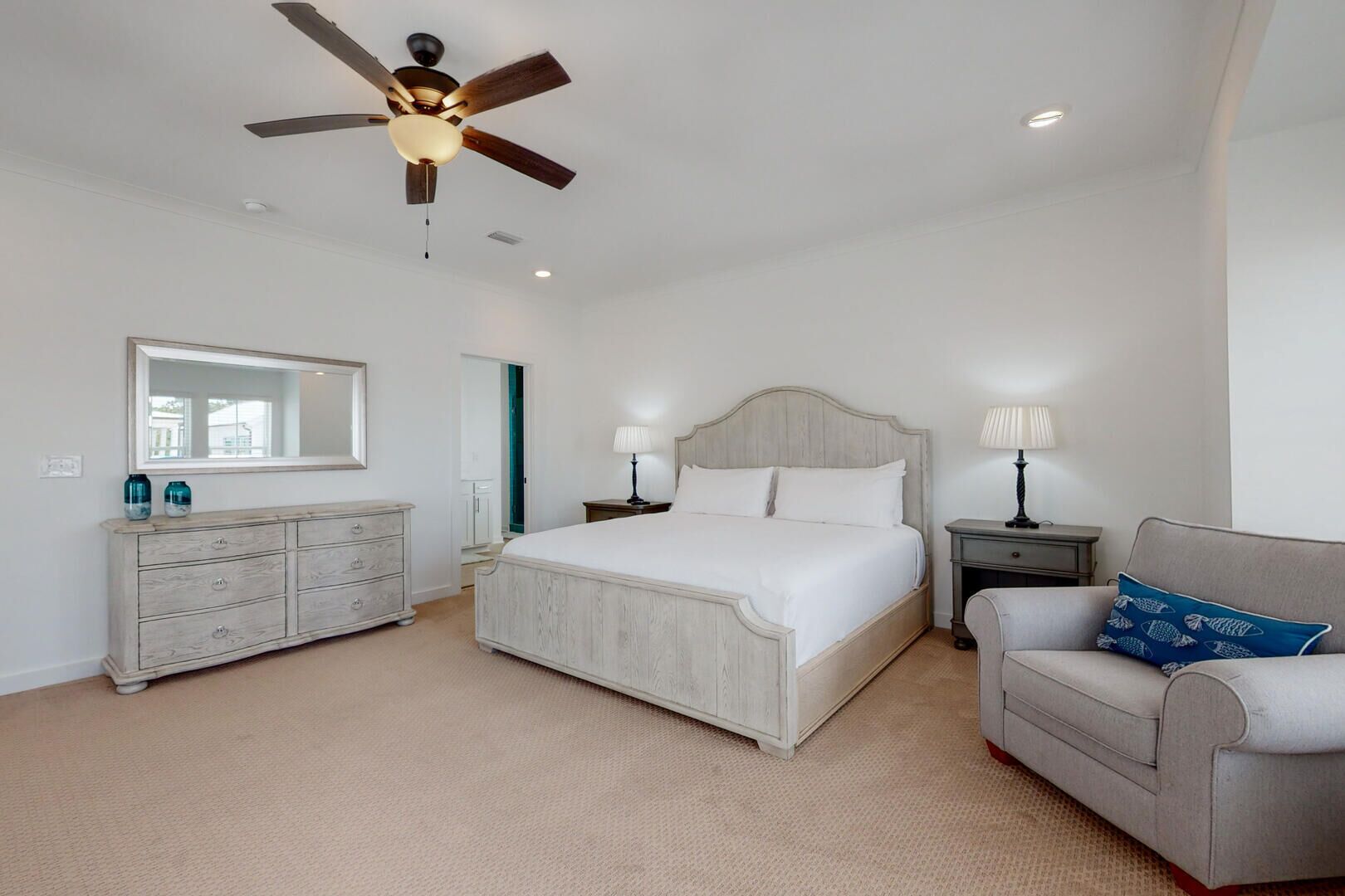 A bedroom with a bed, dresser, nightstands, a sofa, a ceiling fan, and a mirror.