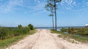 A dirt road leading to a beach with a boat in the distance and a small structure on the right. - Stunning 3br/2.5ba, Pet Friendly, Sleeps 12 (Orange Beach)