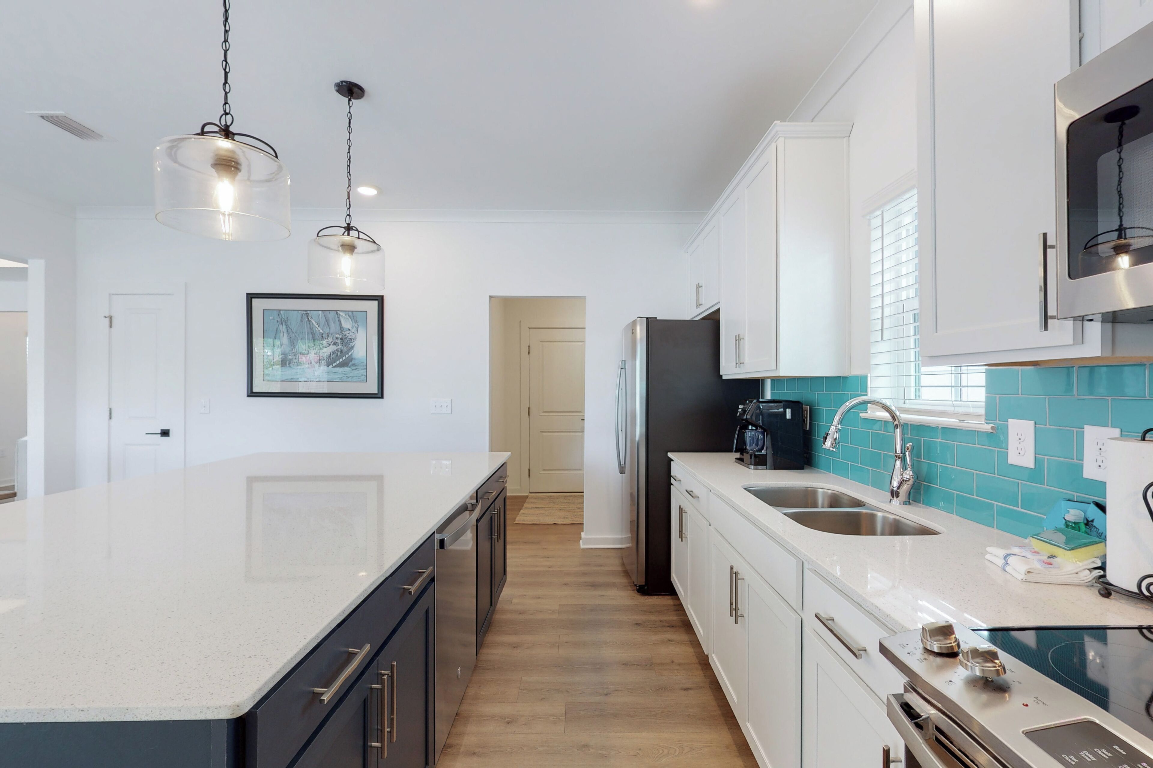A modern kitchen with a large island, stainless steel appliances, and a teal backsplash.