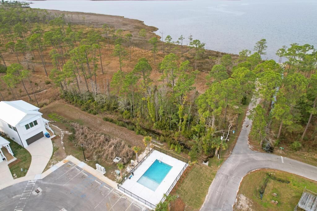 An aerial view of a property with a swimming pool, a white house, and a forested area.
