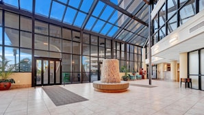 A spacious lobby with a glass ceiling, a central column, and a reception desk. - Beachfront Condo w/ View & Pool, Sleeps 8 (Orange Beach)