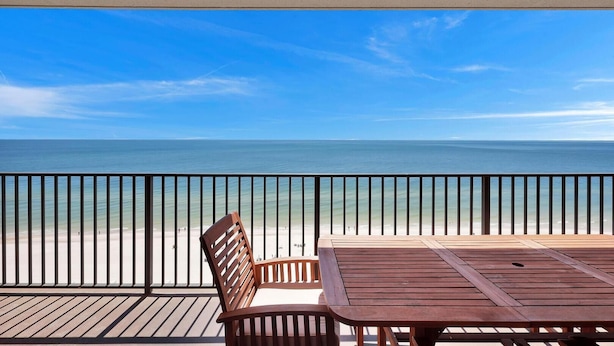 A wooden deck with a table and chairs overlooking a beach. - Beachfront Condo w/ View & Pool, Sleeps 8 (Orange Beach)
