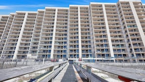 A high-rise residential building with multiple balconies and a pedestrian bridge leading to the beach. - Beachfront Condo w/ View & Pool, Sleeps 8 (Orange Beach)