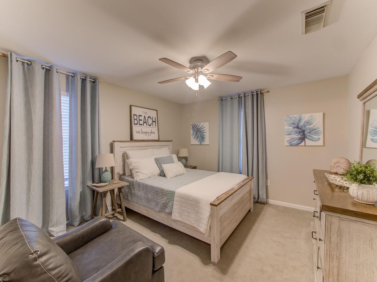 A bedroom with a bed, a ceiling fan, a bedside table with a lamp, a dresser, and a couch.
