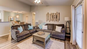 Ein Wohnzimmer mit Deckenventilator, zwei Sofas mit Kissen, einem Couchtisch und einer Essgegend im Hintergrund.