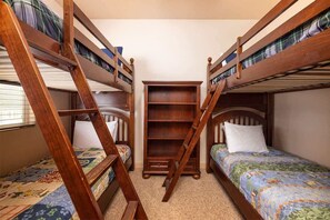 Ein Schlafzimmer mit Etagenbett, Holzleiter, Bücherregal und Fenster mit Jalousien.