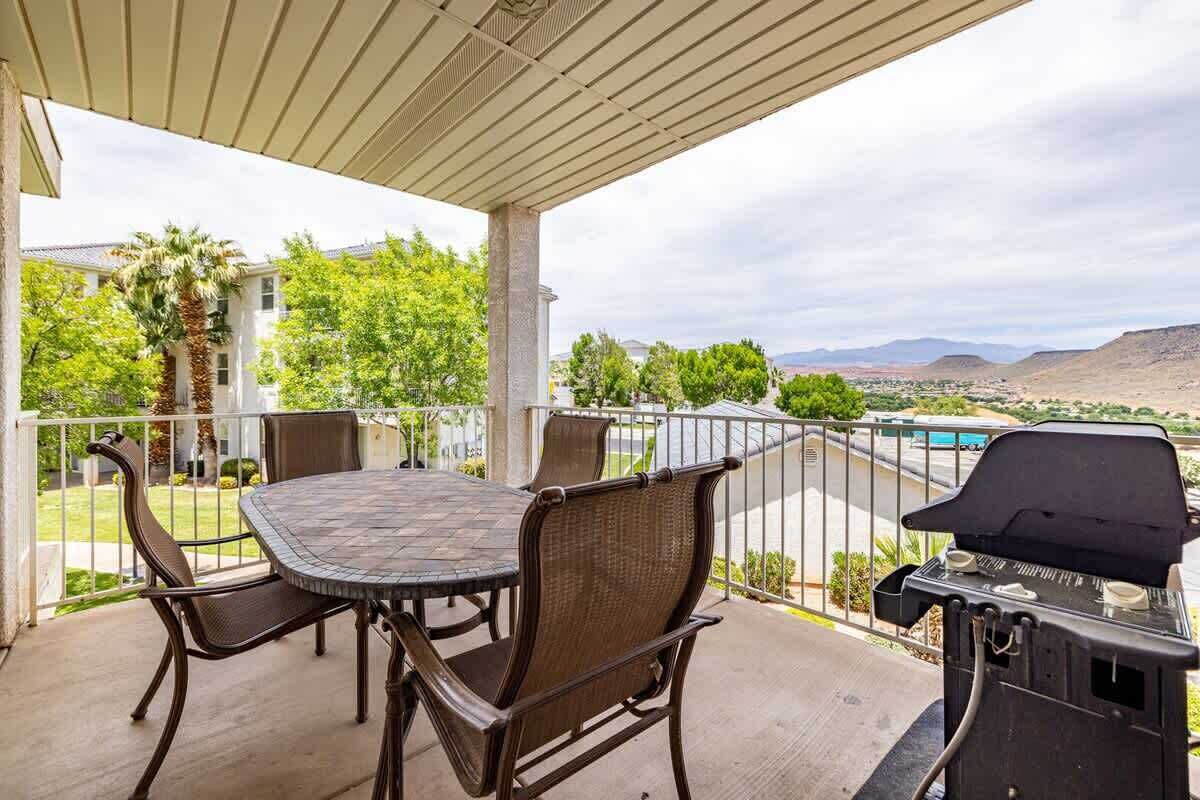 Un patio exterior con mesa y sillas, una parrilla y vistas a una piscina y montañas.