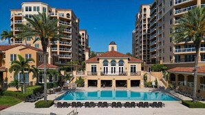 Un hotel con piscina central rodeada de sillones de descanso, palmeras y edificios de varios pisos con balcones.