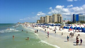 Una playa concurrida, con numerosas sombrillas y gente disfrutando del agua.