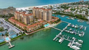 Un puerto deportivo con varias embarcaciones amarradas, rodeado por un gran complejo hotelero con múltiples edificios y una playa al fondo.