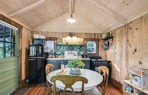 A wooden-paneled kitchen with a refrigerator, microwave, stove, and various kitchen appliances. There is a dining table with chairs and a potted plant.