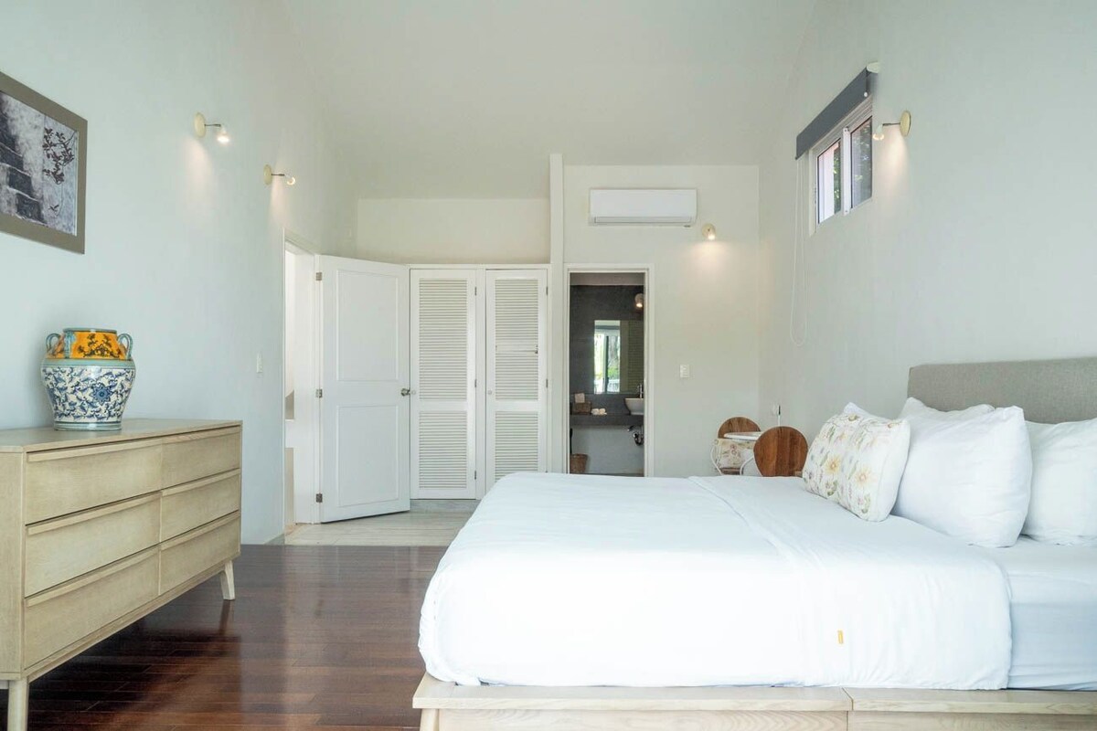 A bedroom with a large bed, a dresser, a wardrobe, and a bathroom visible through an open door.