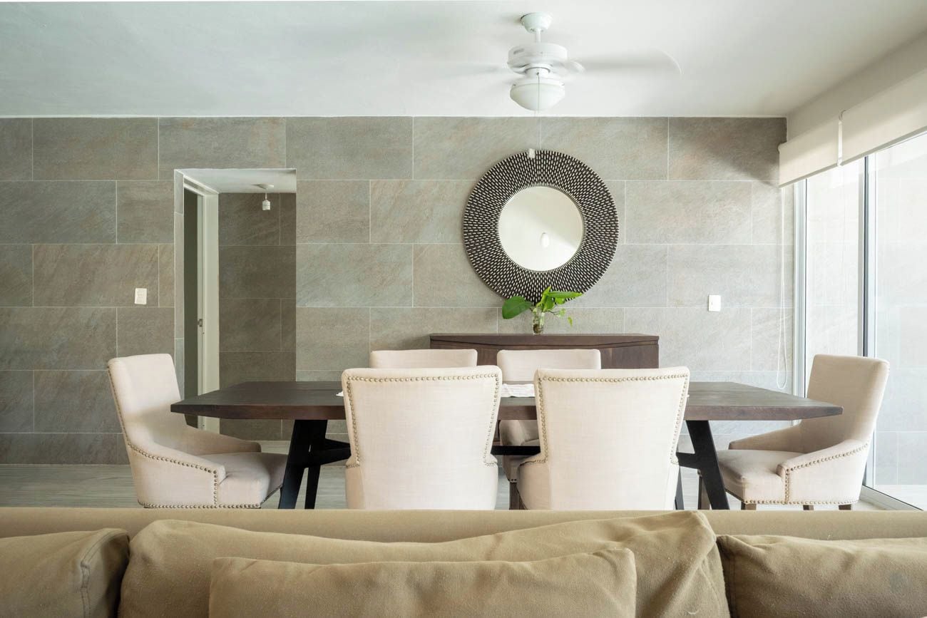 A modern dining area with a round table, six chairs, a decorative mirror, and a ceiling fan.