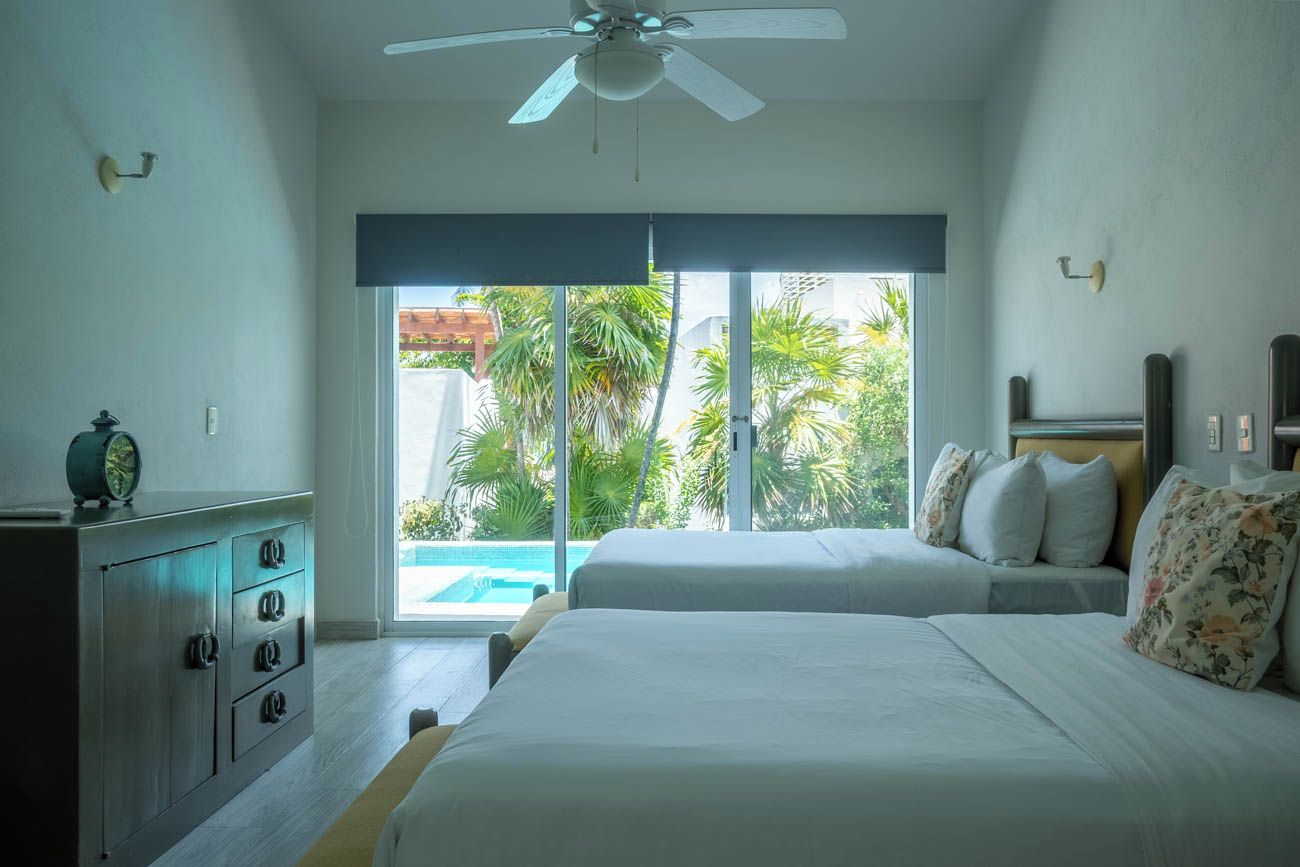 A bedroom with two beds, a ceiling fan, a view of a swimming pool, and a sliding glass door.
