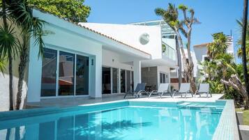 A modern house with a swimming pool, large windows, and a patio with lounge chairs.