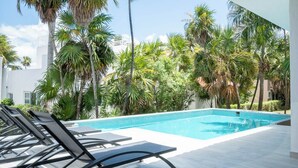 A swimming pool with lounge chairs, surrounded by palm trees and a white building in the background. - Matuk 3 (Playa del Carmen)