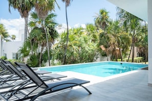 A swimming pool with lounge chairs, surrounded by palm trees and a white building in the background. - Matuk 3 (Playa del Carmen)