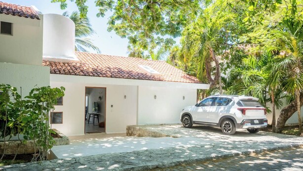 A white building with a tiled roof, a paved driveway, and a parked SUV. - Matuk 3 (Playa del Carmen)