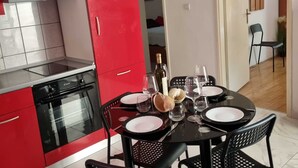 A modern kitchen with red cabinets, a black stove, and a dining area set for four with black chairs and a round table. - Apartments Mavi - Two-bedroom Apartment With Terrace and City View (Dubrovnik)