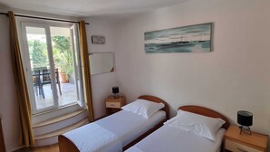 A hotel room with two single beds, a small bedside table with a lamp, a painting on the wall, and a window with curtains. - Apartments Mavi - Two-bedroom Apartment With Terrace and City View (Dubrovnik)