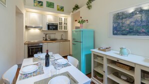 A compact kitchen with white cabinets, a turquoise refrigerator, and a dining area with a table set for two. - Pitti Suite (Florence)