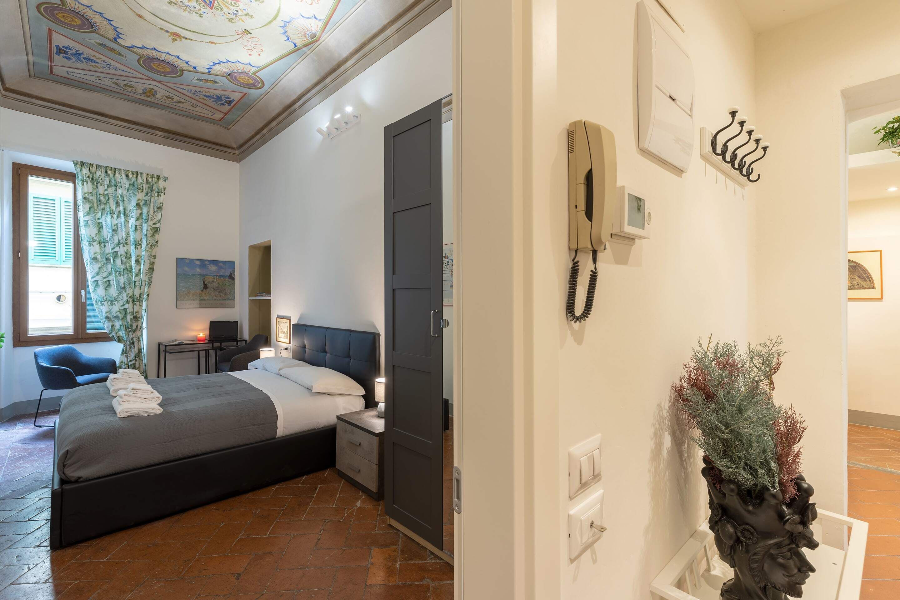 A hotel room with a bed, bedside table, lamp, and a decorative plant.