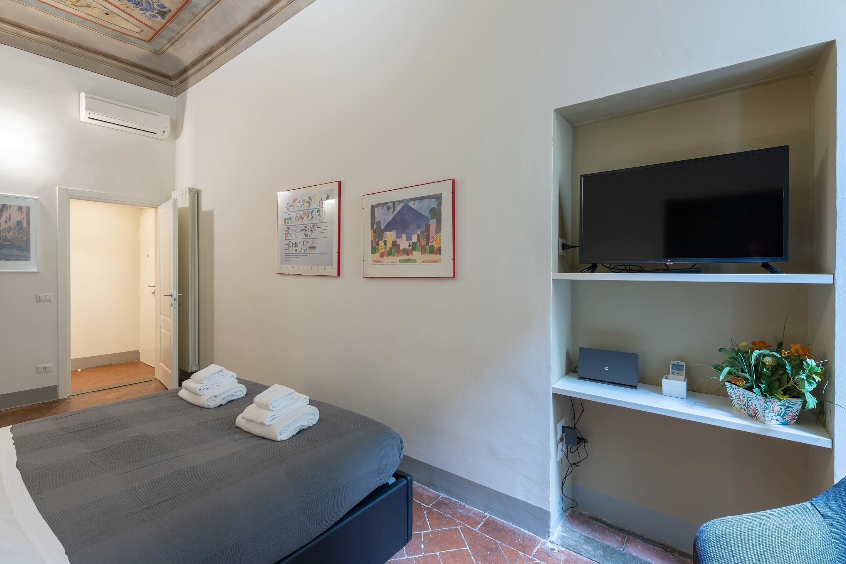 Ein Hotelzimmer mit einem Bett, einem Fernseher auf einem Regal und Kunstwerken an der Wand.